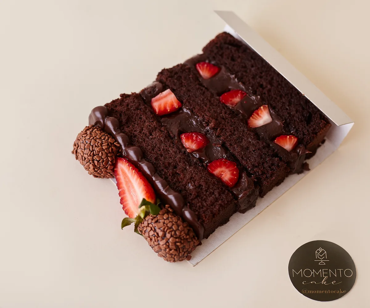 Fatia de bolo de chocolate com morangos e brigadeiros com selo Momento Cake vista de cima
