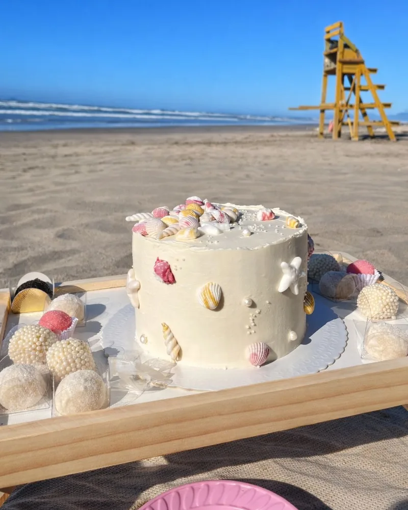 Bolo de aniversário tema praia decorado com conchas de açúcar em piquenique à beira-mar