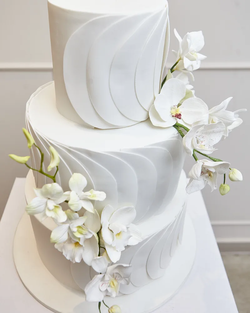 Bolo de casamento de três andares branco plissado com orquídeas em estúdio claro