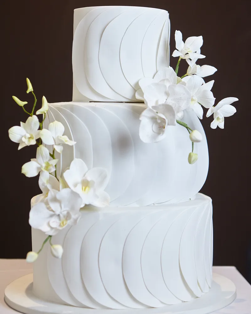 Bolo de casamento branco com orquídeas de açúcar sobre fundo marrom-escuro dramático