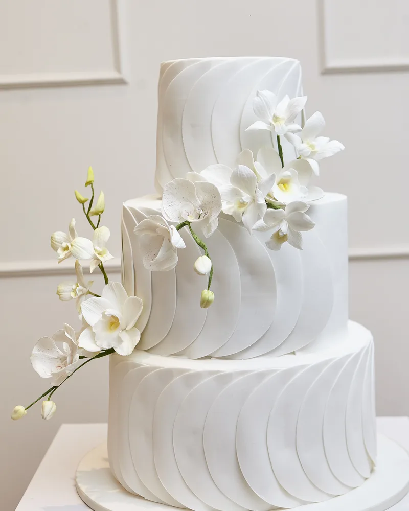 Bolo de casamento completo de três andares com orquídeas em salão de parede creme