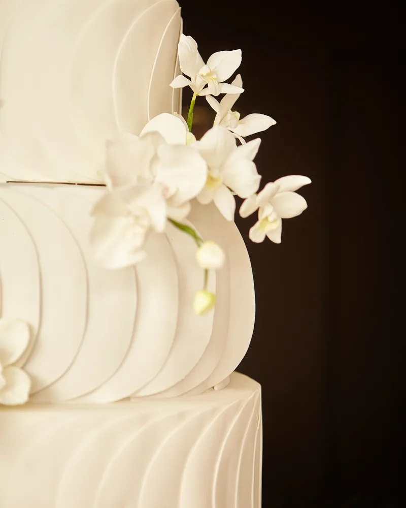 Detalhe dos andares texturizados de bolo de casamento com orquídeas brancas em fundo escuro