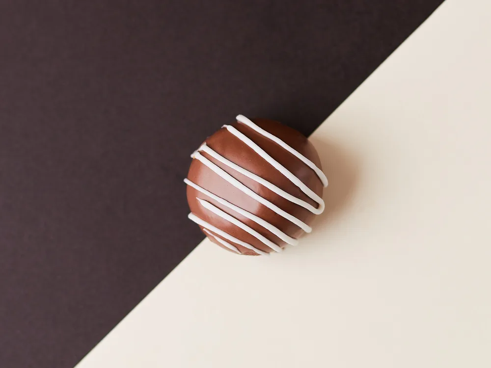 Trufa de chocolate com fios de chocolate branco sobre fundo diagonal marrom e creme
