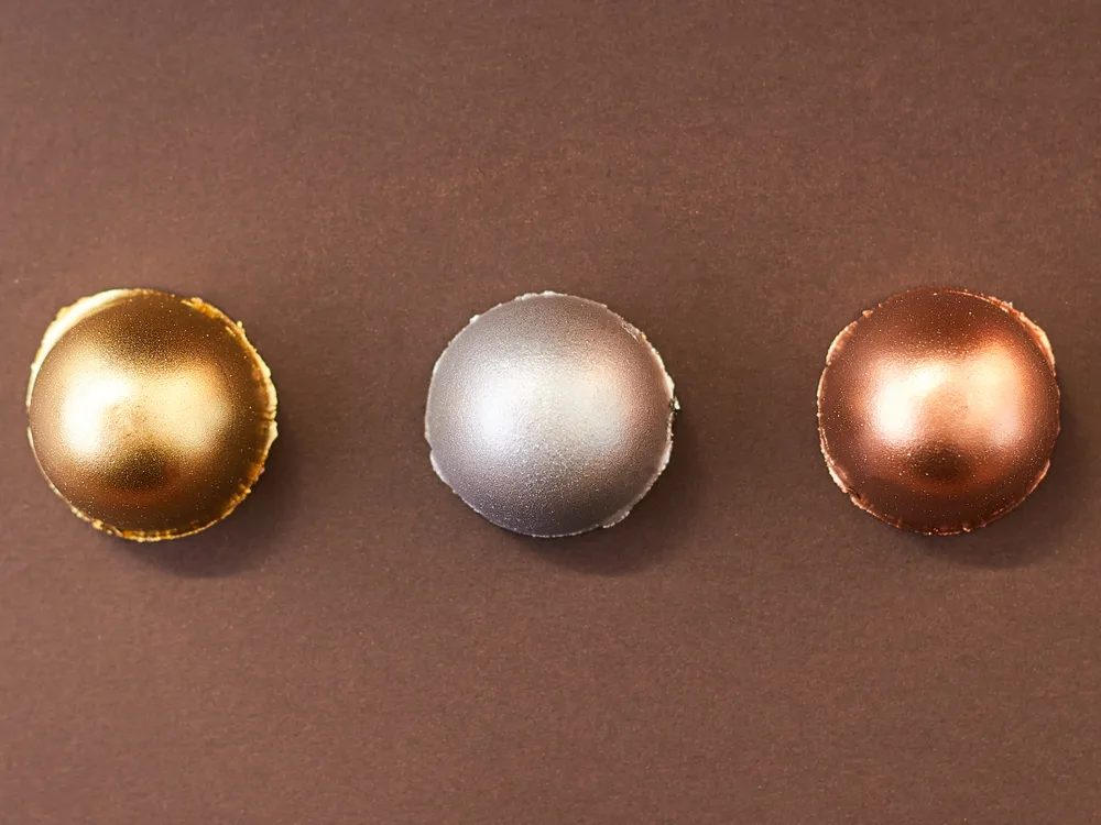Bombons metálicos em ouro, prata e cobre vistos de cima sobre fundo marrom