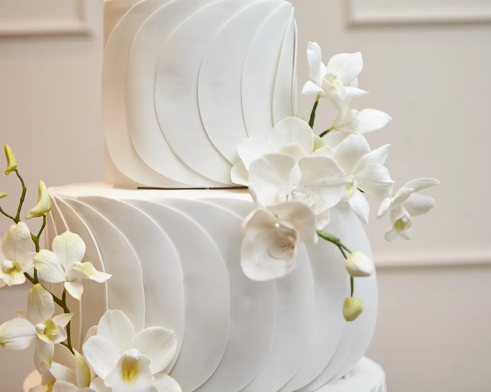 Detalhe de bolo de casamento branco texturizado com orquídeas de açúcar em parede creme