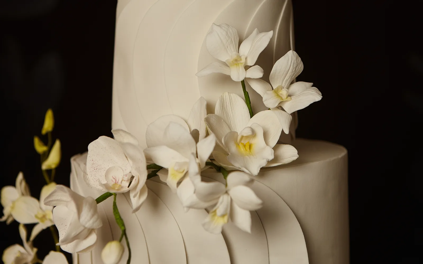 Andares de bolo de casamento com cascata de orquídeas brancas sobre fundo escuro