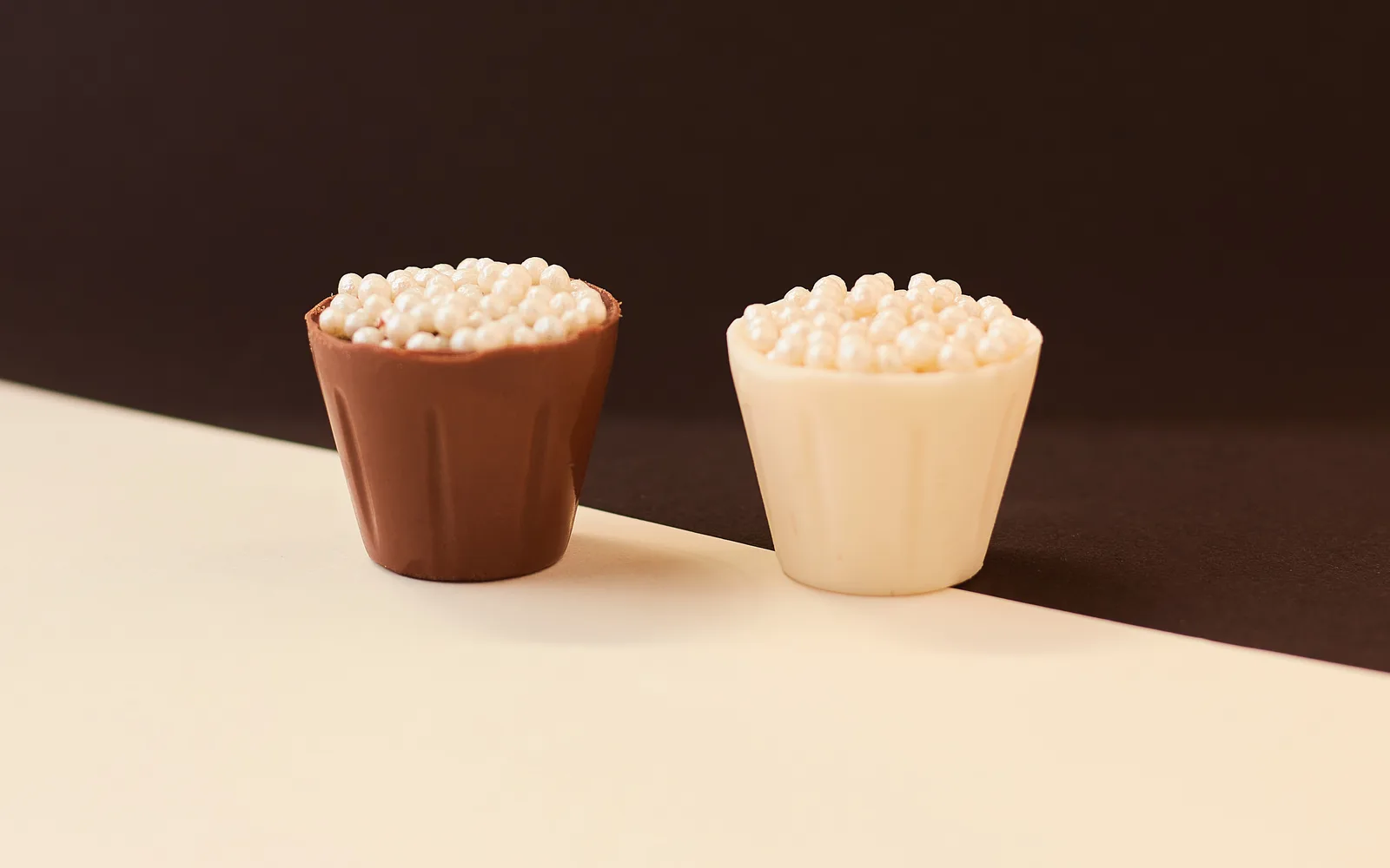 Dupla de copinhos de chocolate com pérolas de açúcar sobre fundo creme e marrom