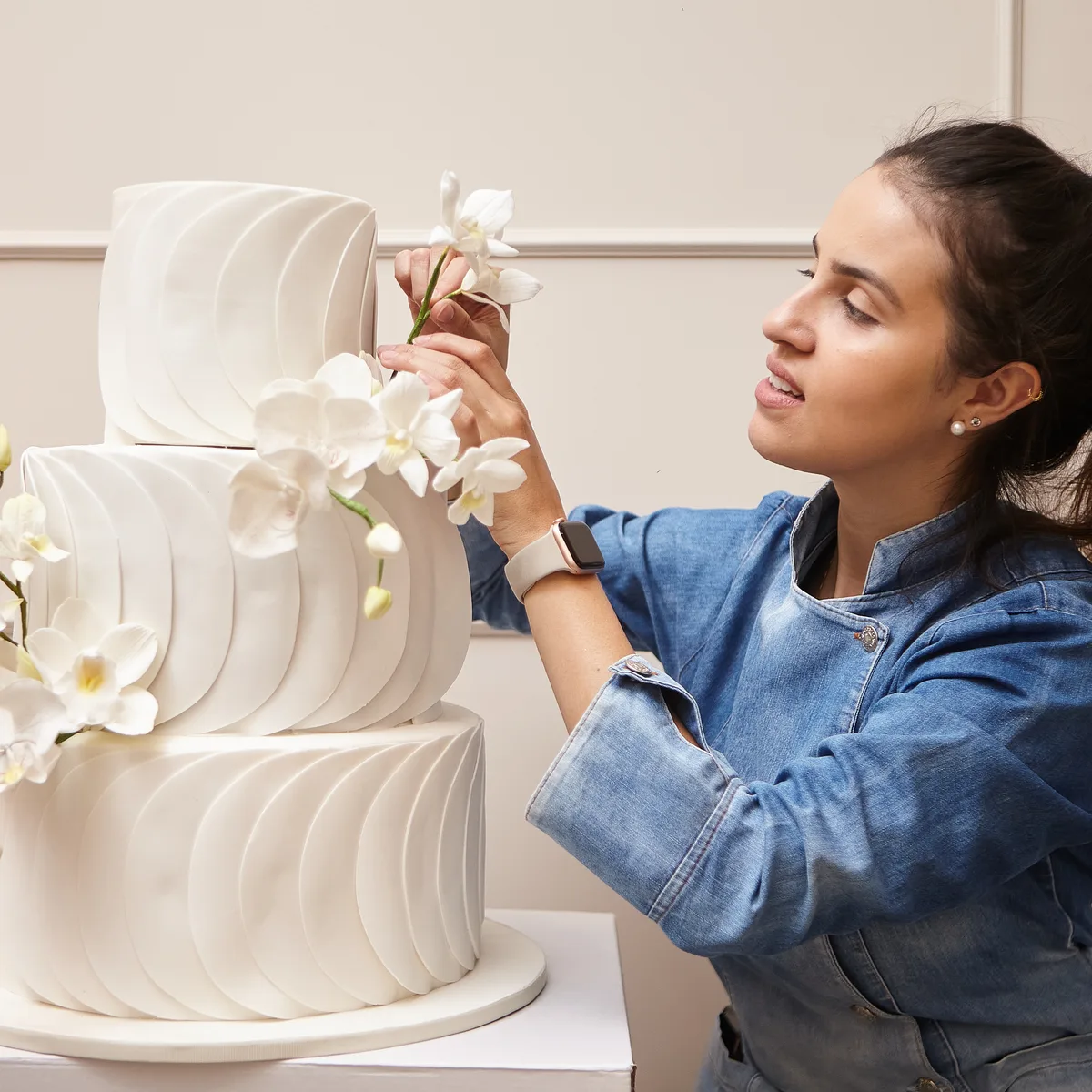 Confeiteira da Momento Cake posicionando orquídea de açúcar no topo de um bolo de casamento