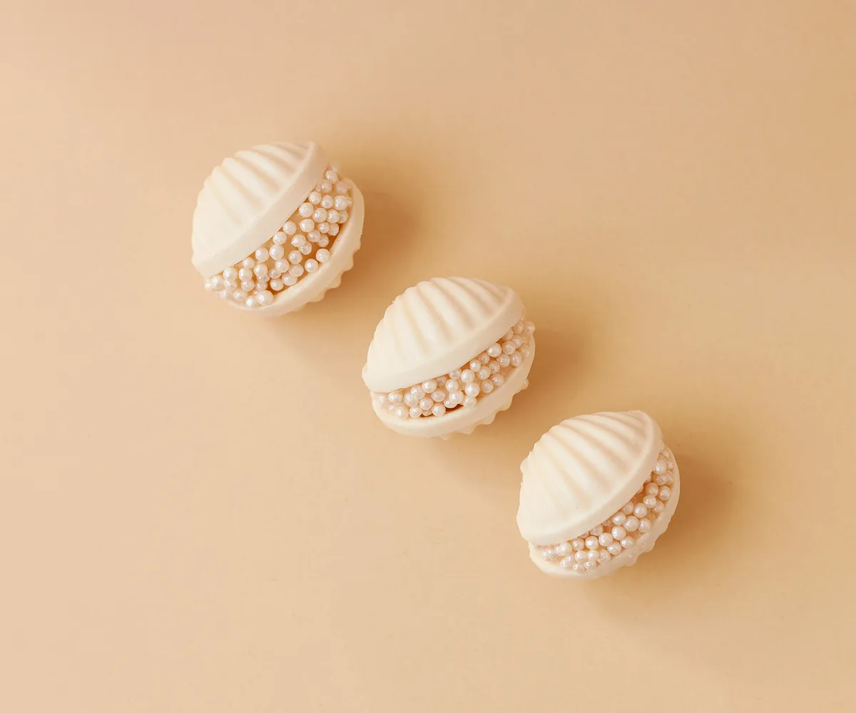 Trio de bombons de chocolate branco com pérolas de açúcar sobre fundo creme delicado