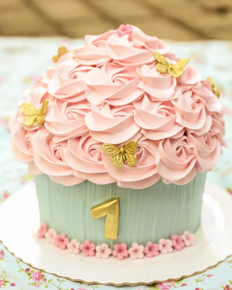 Cupcake gigante com rosas de chantilly rosa, borboletas douradas e número um