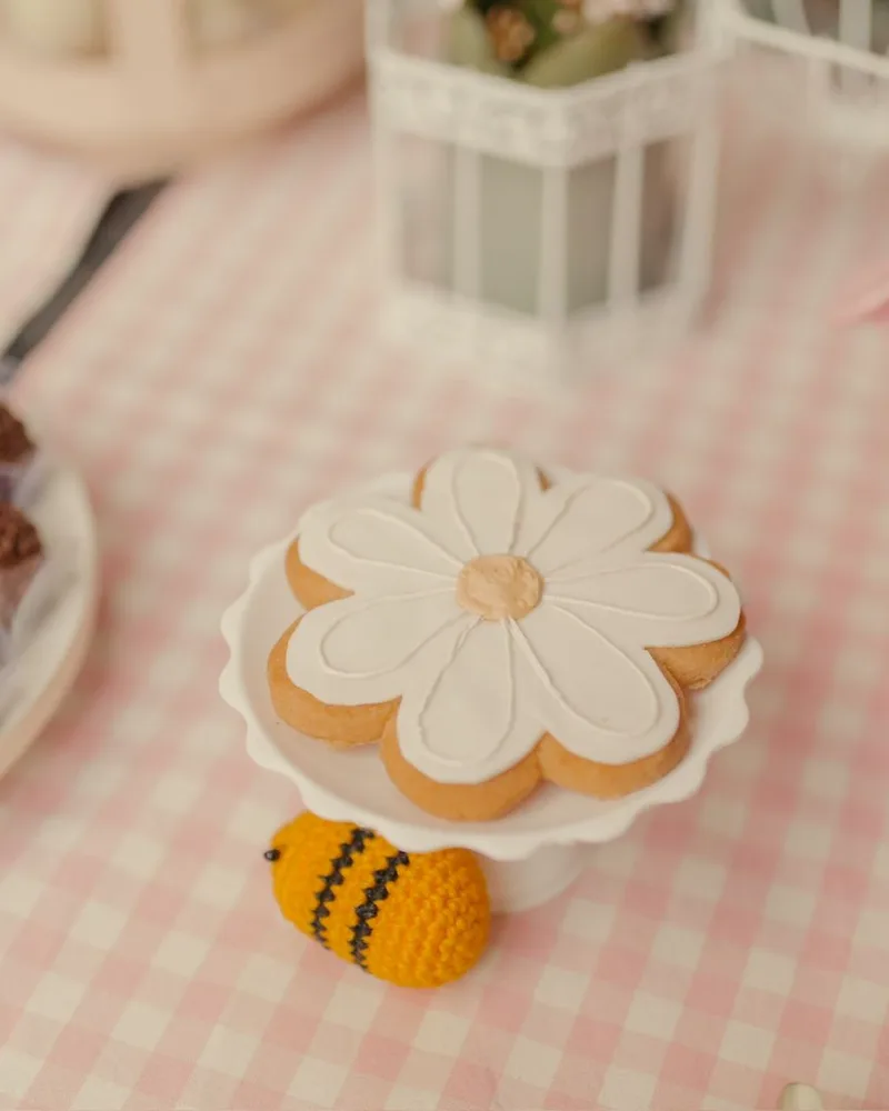 Biscoito decorado de margarida com abelhinha de crochê e brigadeiros em mesa xadrez rosa