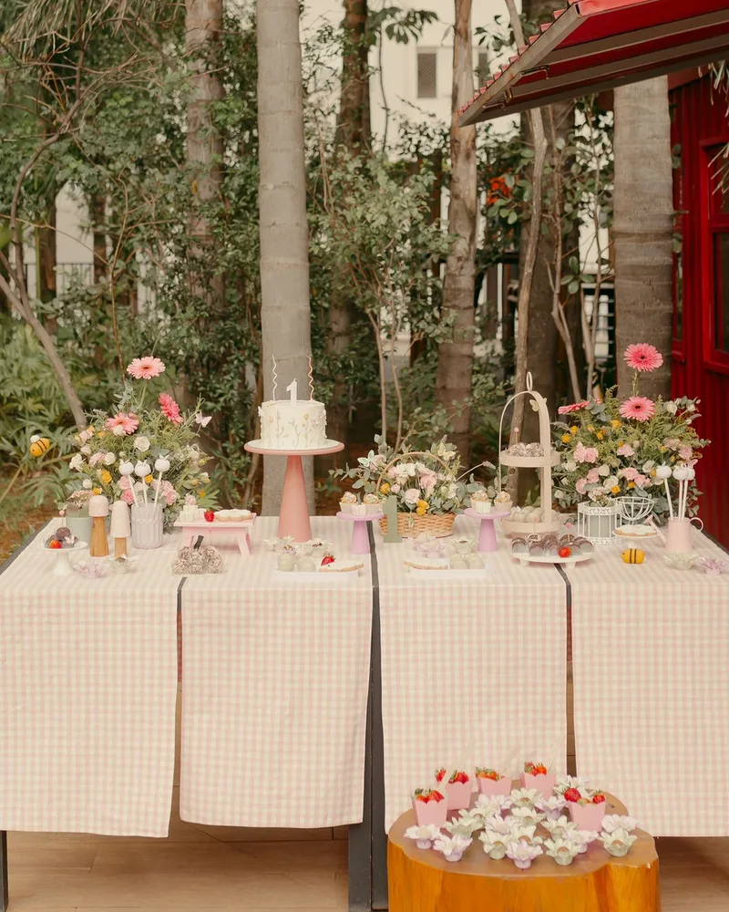 Mesa de doces completa em estilo piquenique no jardim com bolo, flores e toalha xadrez