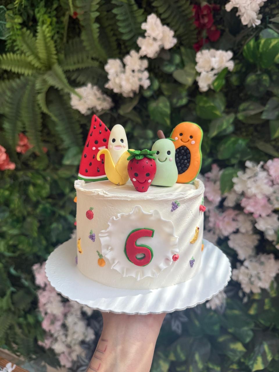 Bolo de mesversário com frutinhas e parede de folhagem