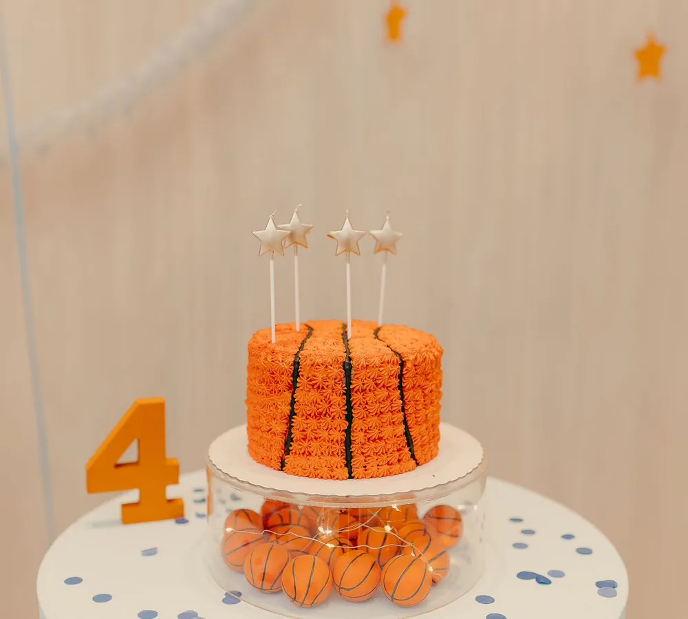 Bolo de aniversário em formato de bola de basquete com velas estrela e mini bolas