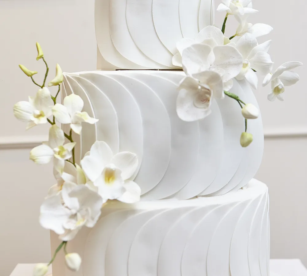 Bolo de casamento de três andares com orquídeas naturais em parede creme com boiserie