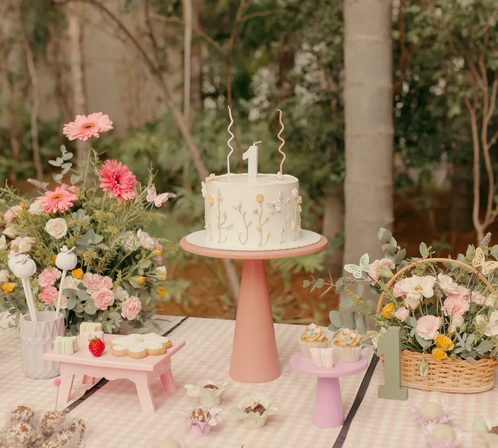 Mesa de doces estilo piquenique no jardim com bolo floral e toalha xadrez rosa